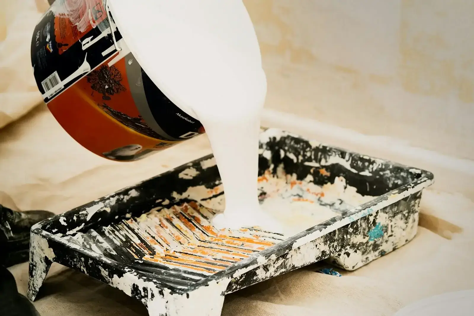 Se está vertiendo pintura blanca en una bandeja para la reforma de una vivienda, lo que muestra los preparativos para un proyecto de pintura.